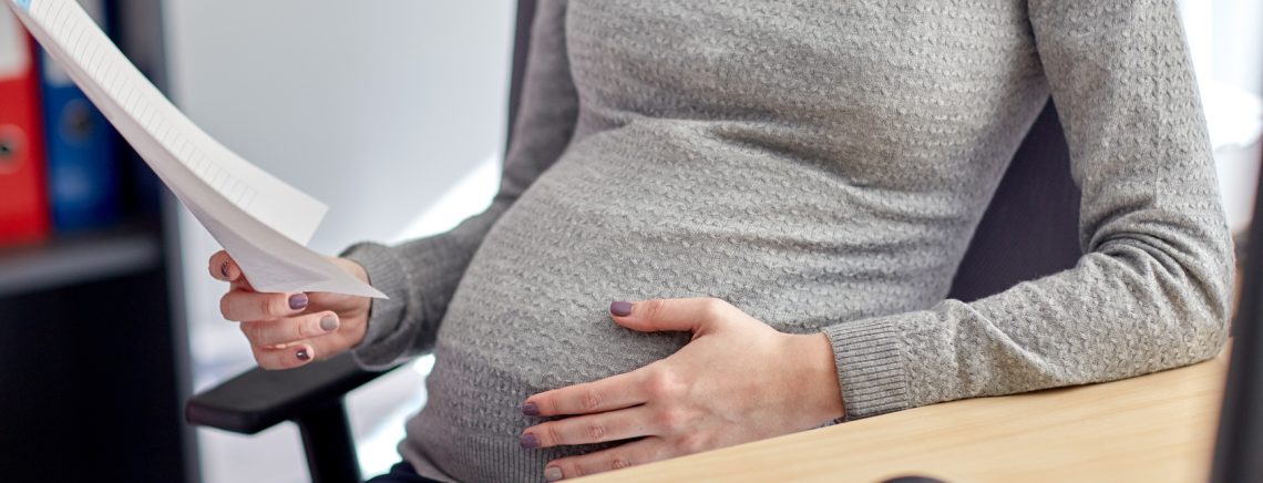 pregnancy, business and work concept - smiling pregnant businesswoman sitting at office table and reading papers