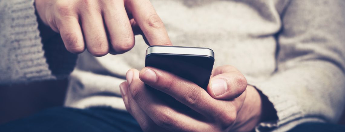 Closeup on a man's hands as he is sitting on a sofa and using a smartphone