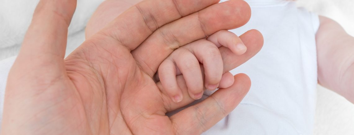 Adoption baby concept. Man holds little child's hand.
