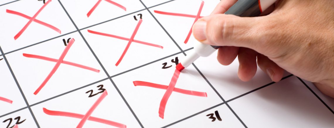 A hand holding a dry erase marker x'ing days of the month off of a calendar.  Passing of time conecpt.